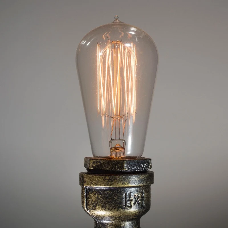 Gros plan d'une ampoule vintage à filament LED allumée, lumière ambrée chaleureuse sur fond sombre