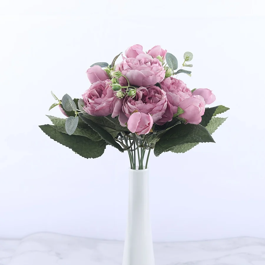 Bouquet de fleurs artificielles roses pivoines aux tons mauves avec feuillage vert dans un vase blanc