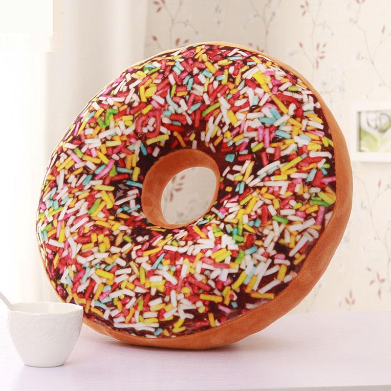 Coussin rond en forme de donut au chocolat avec des vermicelles colorés, posé sur une table près d'une tasse blanche
